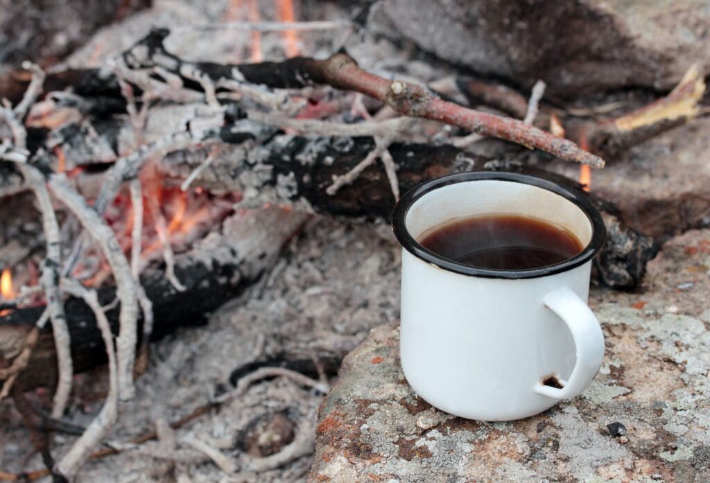 Coffee in metal mug heats up on stone on bonfire.